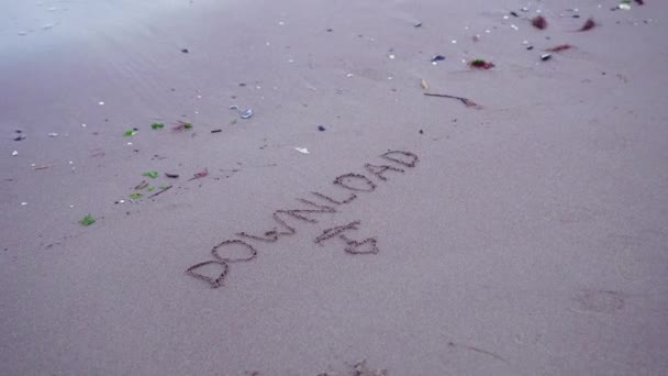 Написанное "Sownload" на песке пляжа — стоковое видео