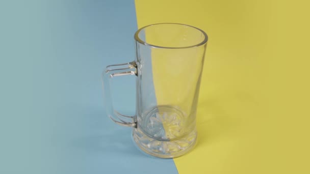 Рух повз скляний кухоль на синьо-жовтому фоні крупним планом — стокове відео