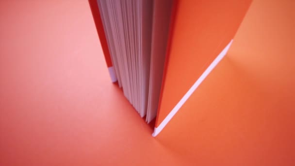 Leicht geöffnetes oranges Buch auf orangefarbenem Hintergrund — Stockvideo