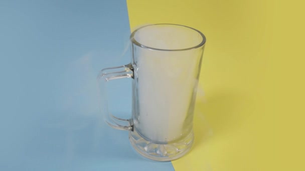 Glass cup full of light smoke on blue and yellow background — Stock Video