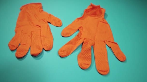 Paar orangefarbene Handschuhe liegen auf türkisfarbener Oberfläche Nahaufnahme — Stockvideo