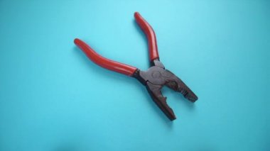 Açık mavi arka planda kırmızı plastik saplı eski pense.