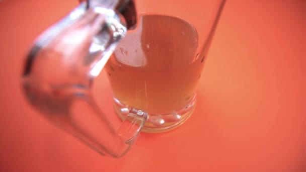 Taza de vidrio con cerveza dorada sobre fondo naranja brillante — Vídeos de Stock