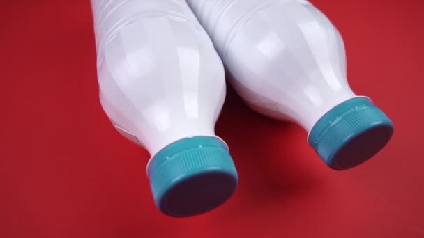 Botellas de plástico blanco con tapas azules sobre fondo rojo — Vídeos de Stock