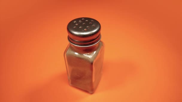 Glass pepper shaker with metal cap turns on orange closeup — Stock Video