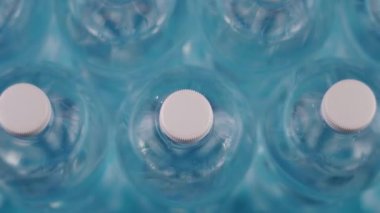 Açık mavi zemin üzerinde temiz su dolu plastik şişeler.