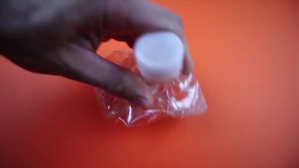 Mann zerknüllt Plastikflasche auf hellorangefarbenem Hintergrund — Stockvideo