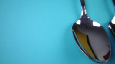 Zarif, parlak gümüş kaşıklar açık mavi arka planda yatıyor.