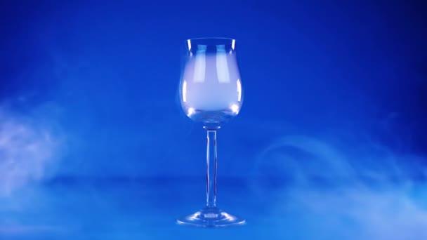 Wijnglas vol stoom staat in vloeiende wolken op blauw — Stockvideo