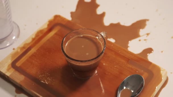 Café marrón en vidrio y derramado en primer plano tablero de madera — Vídeos de Stock
