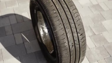 Siyah otomobil tekerleği. İçi su dolu. Kaldırımda yuvarlanıyor.