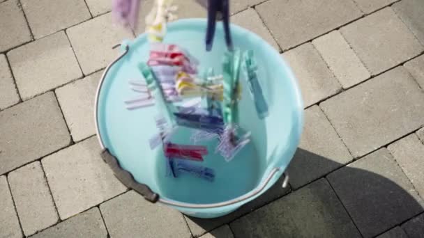 Wäscheklammern in verschiedenen Farben fallen in blauen Eimer — Stockvideo