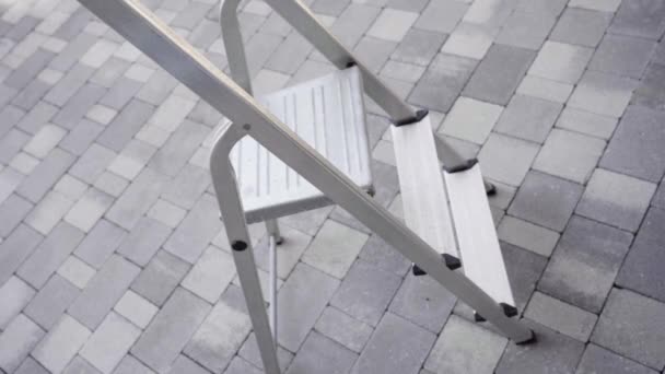 Vrouw vouwt zilver aluminium ladder staan op de stoep — Stockvideo