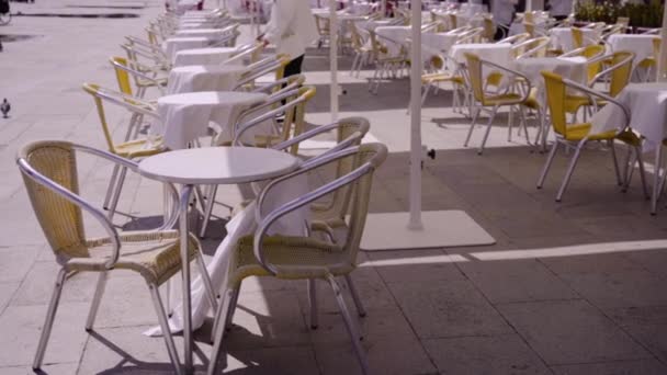 Camarero ajusta sillas por mesas en cafetería en plaza de la ciudad — Vídeo de stock