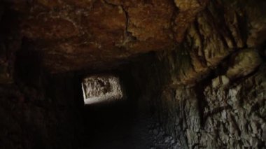 Taş duvarlı tünel ve sonunda güneş ışığı olan tavan.