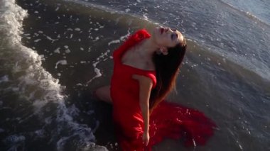 Koyu kırmızı elbiseli esmer, denizde dizlerinin üzerinde duruyor.