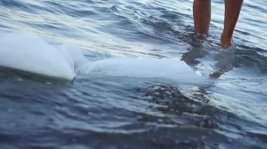 Çıplak ayaklı genç kadın dantelli kumaşın yanında deniz suyunda yürüyor.