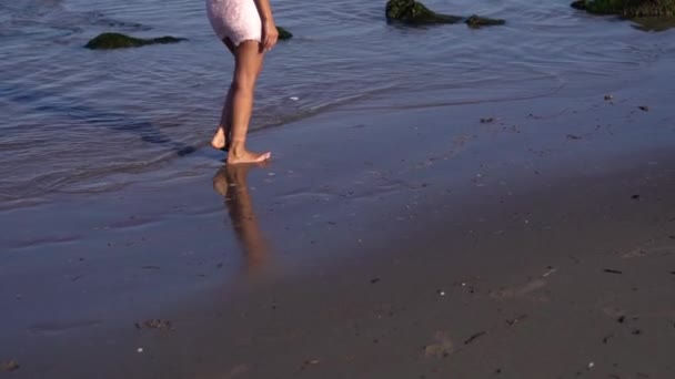 Босиком молодая женщина в розовом платье ходит по мокрому песку — стоковое видео