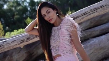 Pembe elbiseli uzun saçlı manken kütüklerin üzerinde oturuyor.