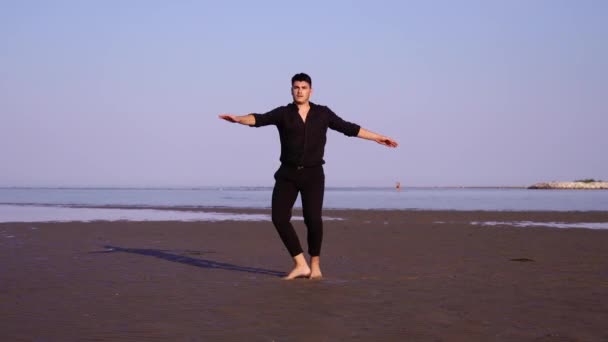 Facet w czerni wykonuje klasyczny taniec baletowy na pustej plaży — Wideo stockowe