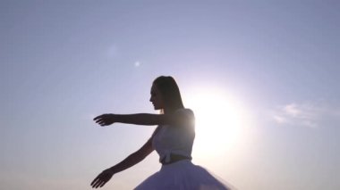 Mavi gökyüzüne el kaldıran etekli kadın silueti.