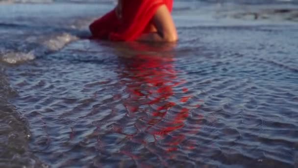 Brünette im roten Kleid mit flauschigen Schleppknien im Meerwasser — Stockvideo