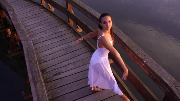 Леди в шифонской юбке танцует балетные упражнения на старом мосту — стоковое видео