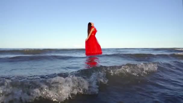 Długowłosa pani w czerwonej sukience stoi w błękitnej wodzie morskiej — Wideo stockowe