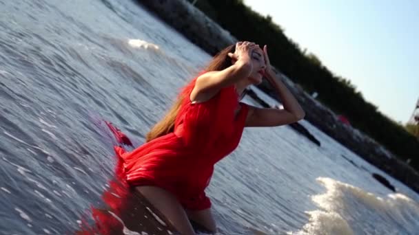 Modelo en vestido rojo se sienta en agua de mar con olas onduladas — Vídeos de Stock