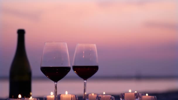 Eleganckie kieliszki z czerwonym winem i świecami na wieczornej plaży — Wideo stockowe
