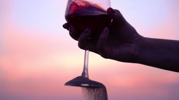 Vrouw schudt wijn giet zand uit glazen voet bij zonsondergang — Stockvideo