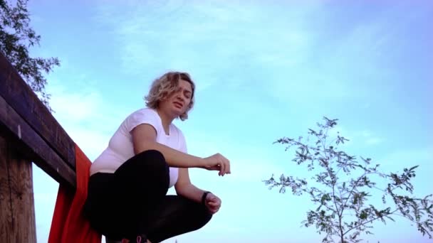 Ung kvinna knäböjer på bänken och äter solrosfrön — Stockvideo