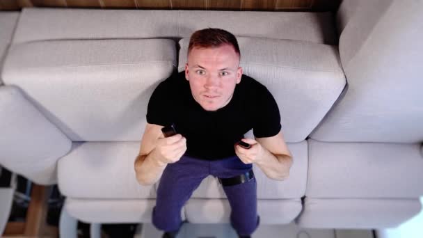 Smiling guy in sportswear lies on sofa upside down shoot — Stock Video