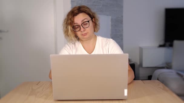 Gözlüklü uykucu sarışın beyaz laptop ekranına bakıyor. — Stok video