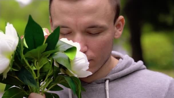 Ο νεαρός άνδρας μυρίζει λουλούδια για να αλλάξει το χρώμα των ματιών σε ροζ. — Αρχείο Βίντεο