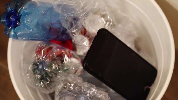 Zwarte smartphone valt in vuilnisbak met plastic afval — Stockvideo