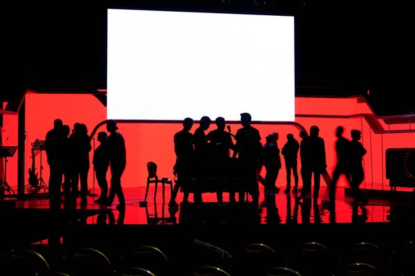 Silhouette of an people on the stage in the front of a colorful background.