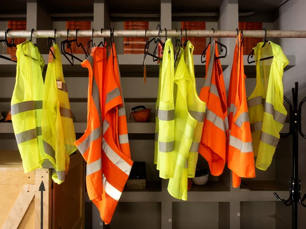 yellow work vests are hanging on a hanger. Hardhats and safety jackets on hanger.