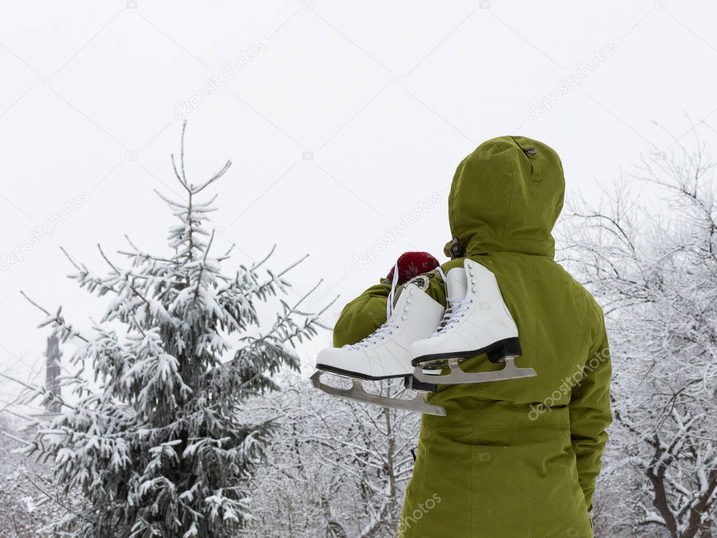 Woman with white ice skates looks at the snow-covered spruce