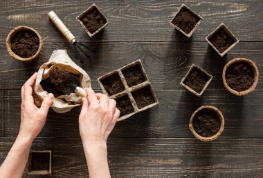 Kadın çevre dostu çömleklere toprak döküyor.