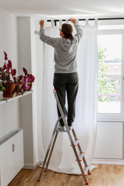 Kadın perde çubuğuna beyaz perdeler asıyor
