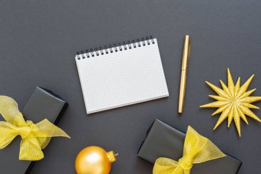 Tatil arka planı, simli altın yıldızlı siyah arkaplan ve hediye kutuları, sarmal not defteri ve kalem, düz yatış, üst görünüm, boşluk kopyala