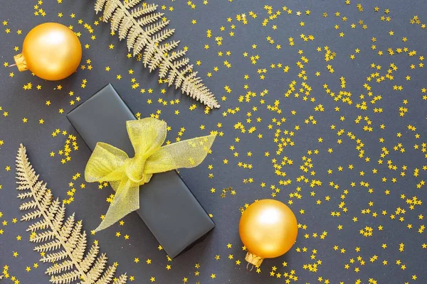Festive background with gold decorations , shiny golden fern leaves and gift box with christmas balls on a black background with glitter gold stars , flat lay, top view, copy space