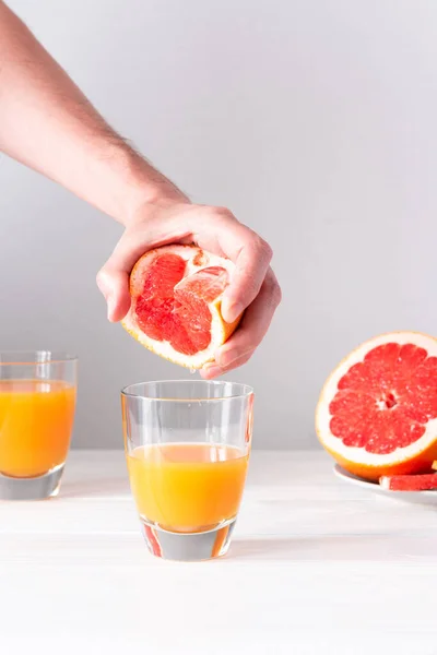 Male hand squeezes grapefruit juice in a glass with orange juice, summer refreshing citrus drink