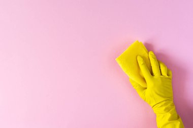 Pembe arka planda temizlik süngeri olan sarı lastik bir eldiven verin.