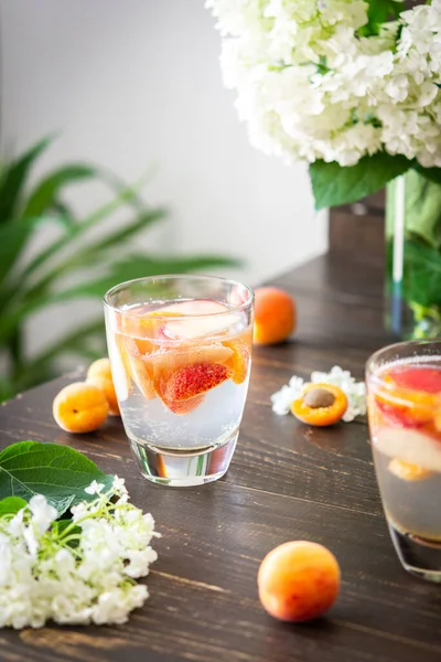 Refreshing drink with apricots and peaches, cold sparkling water with fruits, a vase of flowers viburnum opulus Roseum and a glass with a drink