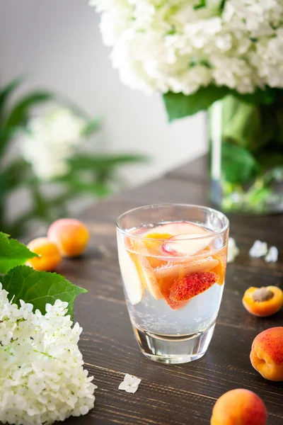 Refreshing drink with apricots and peaches, cold sparkling water with fruits, a vase of flowers viburnum opulus Roseum and a glass with a drink