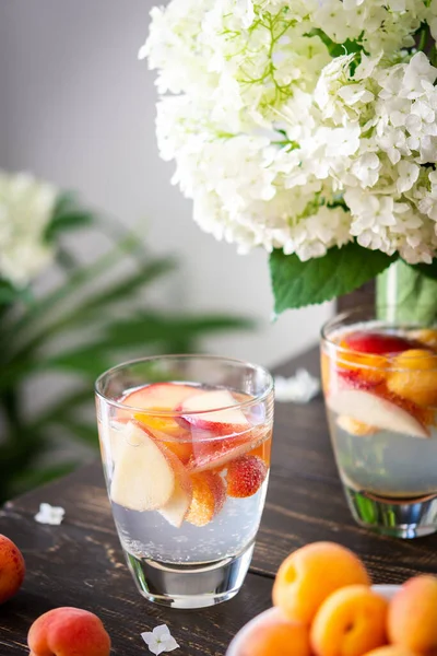 Refreshing drink with apricots and peaches, cold sparkling water with fruits, a vase of flowers viburnum opulus Roseum and a glass with a drink