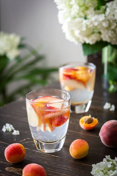 Refreshing drink with apricots and peaches, cold sparkling water with fruits, a vase of flowers viburnum opulus Roseum and a glass with a drink