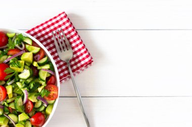 Taze olgun domates salatası, soğan, avokado, salatalık, maydanoz ve zeytinyağı, beyaz bir tabakta salata, çatal ve havlu ile beyaz ahşap arka planda.